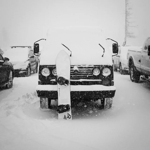 A snowboard leaning against a snowed-in Land Rover